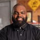 A black man with a beard in a black shirt.