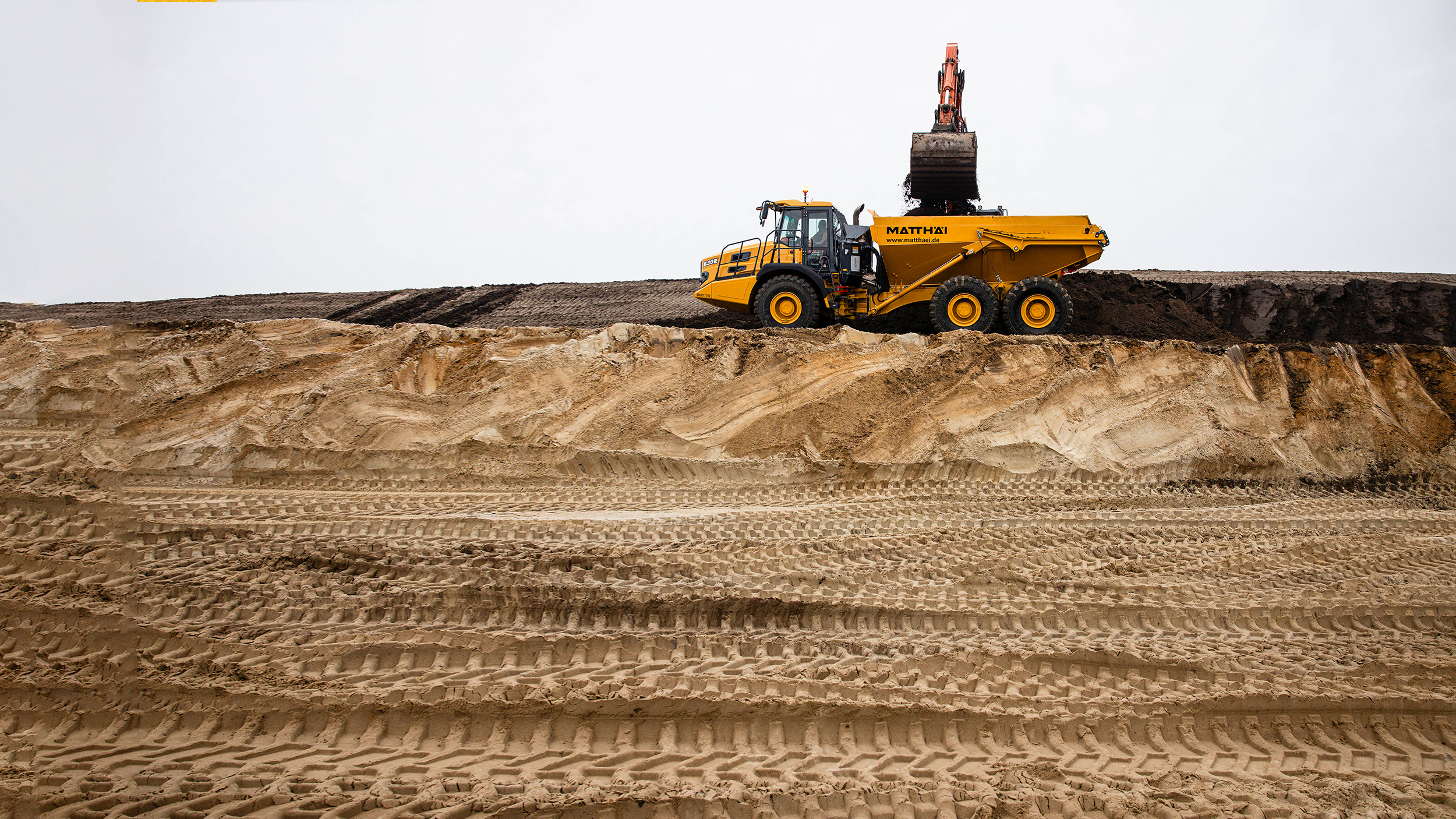 A yellow dump truck on a sand hill.